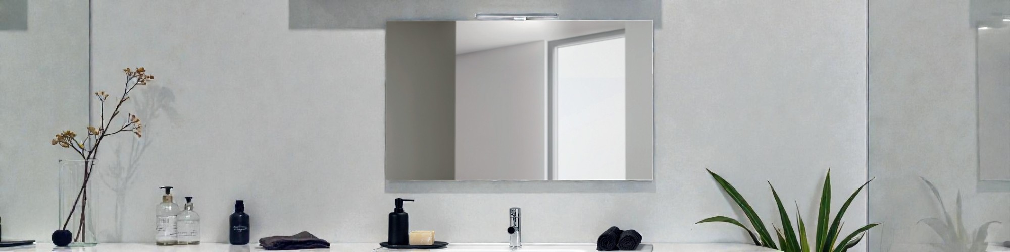 Miroir rectangulaire au-dessus d’un lavabo moderne avec distributeur, serviettes foncées et plante décorative sur un plan de salle de bain minimaliste.